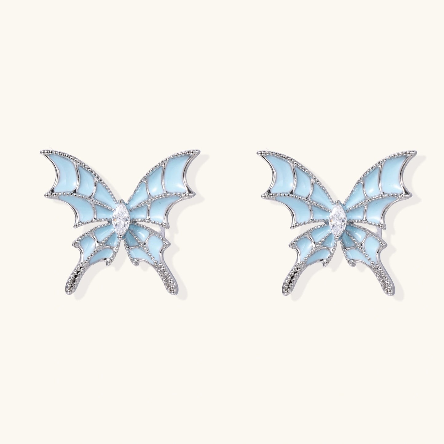 Long silver-tone earrings with powder blue enamel butterfly studs and flowing chain tassels on cream background
